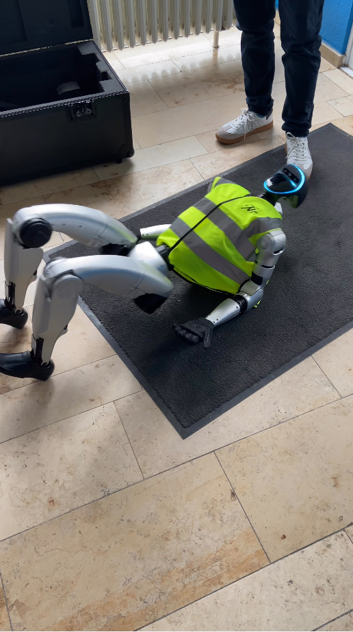 A humanoid robot in a safety vest performs tasks on a mat, showcasing technology in a modern workspace environment.