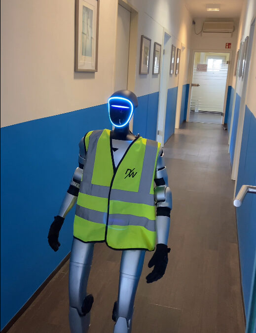 A humanoid robot in a reflective vest walking down a hallway with blue walls and framed artwork.