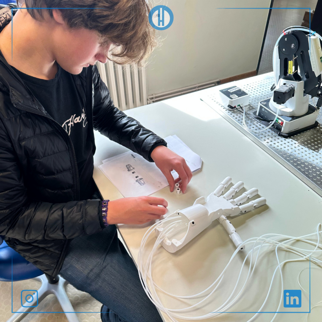A young person assembles a prosthetic hand prototype on a table, focusing on connecting parts and following instructions.