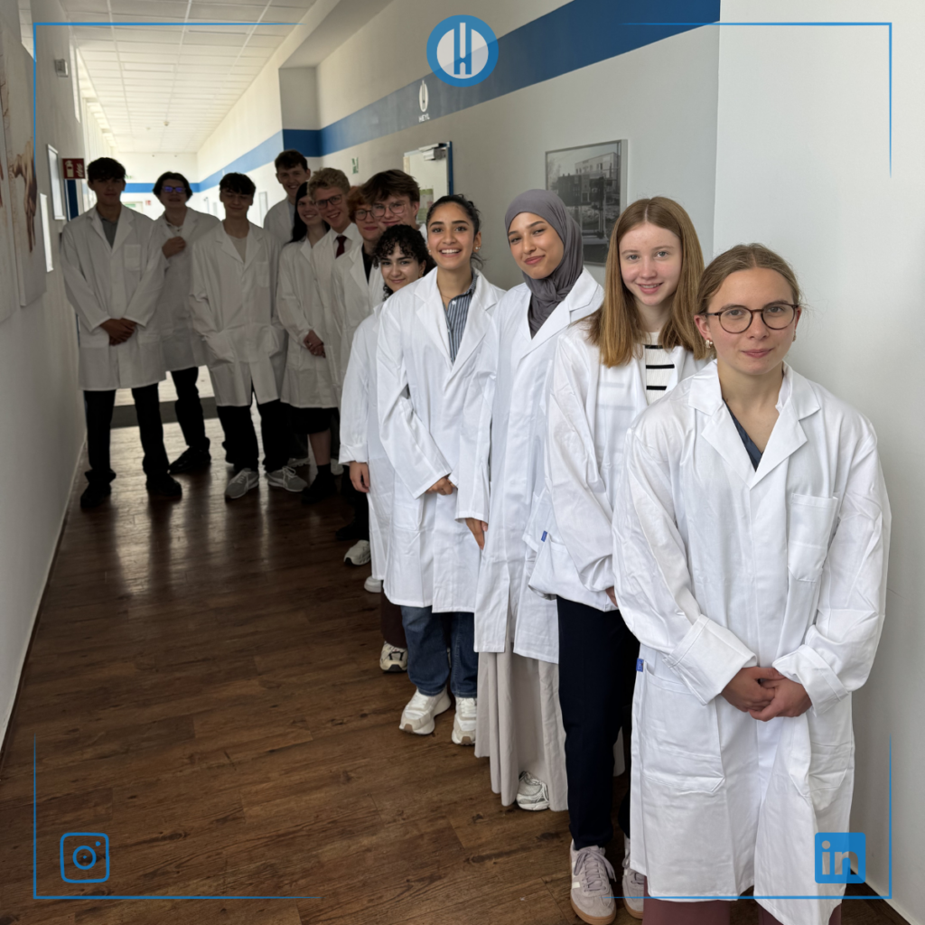 Students in white lab coats stand in a hallway, ready for a science experiment or class activity.