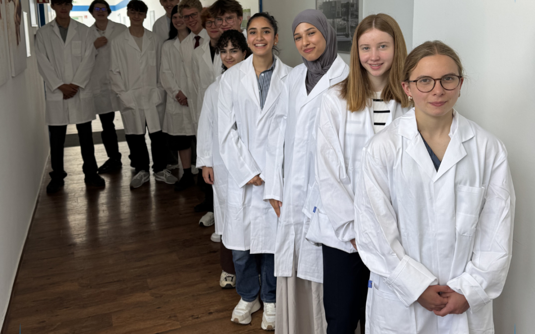 Students in white lab coats stand in a hallway, ready for a science experiment or class activity.